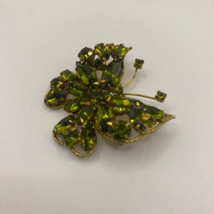 May include: A gold-tone butterfly brooch with green rhinestones. The brooch is in the shape of a butterfly with its wings spread out.