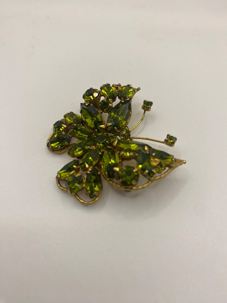 May include: A gold-tone butterfly brooch with green rhinestones. The brooch is in the shape of a butterfly with its wings spread out.