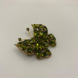 May include: A gold-toned butterfly brooch with green rhinestones. The brooch is made of metal and has a detailed design.
