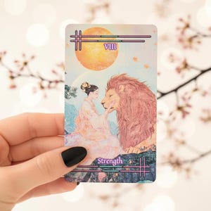 May include: A rectangular tarot card featuring the Strength VIII arcana. The illustration depicts a person in light-colored robes gently touching the face of a large lion. A bright orange sun hangs in the sky above a mountainous landscape.