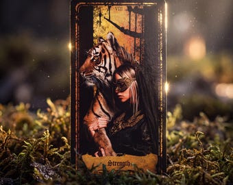 May include: A rectangular tarot card labeled Strength with the Roman numeral VIII, featuring an illustration of a person wearing a gold mask standing beside a tiger. The card has a dark border and a textured, weathered-looking bottom section.