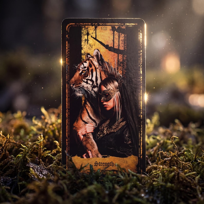 May include: A rectangular tarot card labeled Strength with the Roman numeral VIII, featuring an illustration of a person wearing a gold mask standing beside a tiger. The card has a dark border and a textured, weathered-looking bottom section.