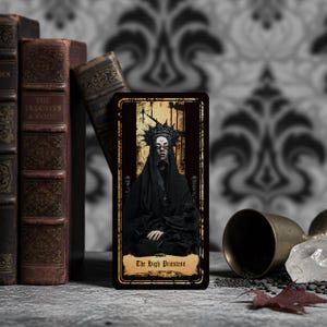 May include: A rectangular tarot card titled The High Priestess featuring a figure in a black hooded robe and a dark spiked crown. The card has a gold-toned border and a distressed, aged appearance with a dark, moody color palette and Roman numeral II.