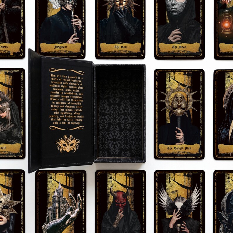 May include: A black rectangular storage box with a hinged lid, featuring gold text and a mask emblem on the interior. The box is surrounded by multiple tarot cards displaying dark, gothic-style illustrations of figures in masks, robes, and ornate headpieces.