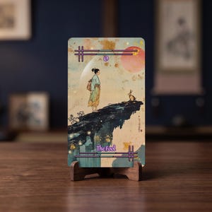 May include: A rectangular tarot card titled The Fool, featuring an illustration of a person standing on a cliff edge with a rabbit. The artwork uses a muted color palette of beige, blue, and orange, with a large moon and sun in the sky.