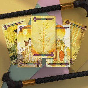 May include: A collection of four tarot cards featuring yellow and gold illustrations, including the Ace of Wands, Queen of Wands, King of Wands, and the Nine of Wands, positioned between two black walking canes with gold-toned metal collars.