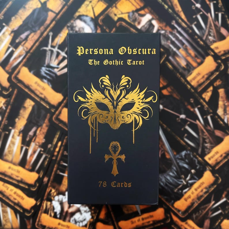 May include: A black rectangular tarot deck box with gold foil lettering that reads Persona Obscura The Gothic Tarot. The box features a gold foil mask illustration and an ankh symbol, with the text 78 Cards printed at the bottom.