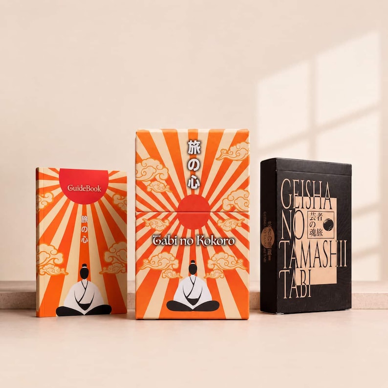 May include: Two rectangular boxes and a guidebook featuring orange and cream sunburst patterns with stylized clouds and a figure in a seated pose. The central box displays the text Tabi no Kokoro, while the black box is labeled Geisha no Tamashii Tabi.