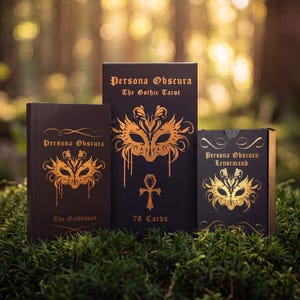 May include: Three black rectangular boxes with gold foil detailing. The left box is labeled Persona Obscura The Guidebook, the center box Persona Obscura The Gothic Tarot 78 Cards, and the right box Persona Obscura Lenormand, all featuring mask art.