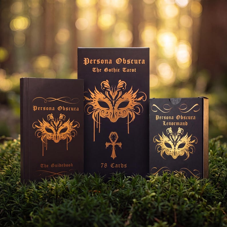 May include: Three black rectangular boxes with gold foil detailing. The left box is labeled Persona Obscura The Guidebook, the center box Persona Obscura The Gothic Tarot 78 Cards, and the right box Persona Obscura Lenormand, all featuring mask art.