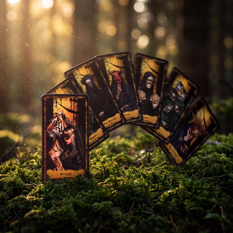 May include: A fan of rectangular tarot cards with dark, gold-bordered illustrations. The front card features a tiger and a person with the text Strength. Other visible cards display figures including a devil, a hooded person, and various symbolic imagery.
