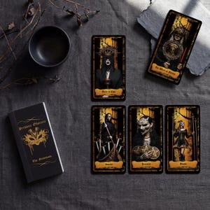 May include: A tarot deck set featuring a black guidebook titled Persona Obscura with a gold mask graphic and five rectangular tarot cards. The cards display dark, detailed illustrations of figures in masks and robes with gold and black color schemes.