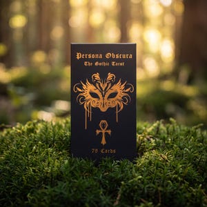 May include: A black rectangular tarot deck box titled Persona Obscura The Gothic Tarot with 78 Cards printed in gold. The box features a gold ornate mask illustration and an ankh symbol centered on the front cover with metallic gold lettering.