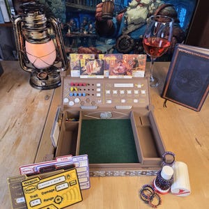 May include: A tabletop role-playing game setup featuring a wooden game board with a green felt surface, cards, dice, and tokens. A vintage oil lamp and a glass of red wine are also present. A fantasy art print hangs in the background.