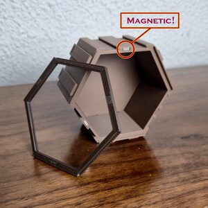 May include: A brown, geometric, hexagonal box with a clear, hinged door. The door is open, revealing the interior. The word "MAGNETIC!" is written above the box, with an arrow pointing to a small, rectangular magnet.