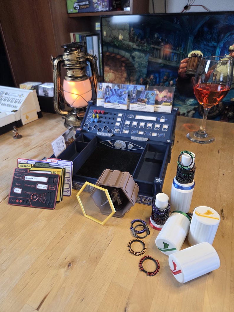 May include: A tabletop scene featuring a blue game organizer, game cards, and various game accessories. A vintage-style lantern with a lit bulb sits nearby. Several white cylindrical containers with colored accents are also present.