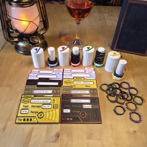 May include: A collection of tabletop gaming accessories, including white cylindrical tokens with colored accents, game cards, and rings. The tokens have red, green, yellow, and blue details. The cards are black and yellow with text. A glass of wine and a lantern are also present.