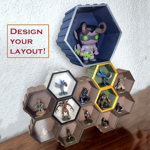 May include: Hexagonal display shelves in brown, blue, and yellow, showcasing various figurines. The shelves are mounted on a white wall, with the text "DESIGN YOUR LAYOUT!" in a red box. The shelves are designed to hold collectibles.