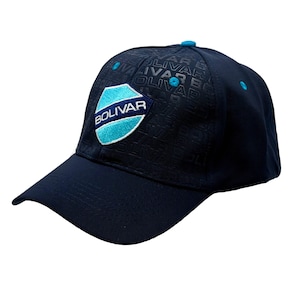 Puede incluir: Gorra de béisbol azul marino con un escudo con la palabra "Bolivar". La gorra tiene una visera curva y un pequeño botón. La palabra "Bolivar" también está impresa en la tela de la gorra.