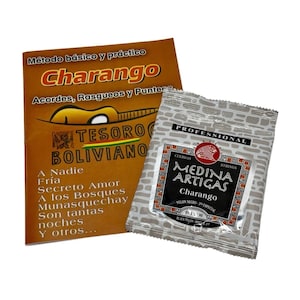 May include: Two items: a brown book titled "Charango" with Spanish text and a silver package of "Medina Artigas Charango" strings. The book has a guitar illustration and the package has a red fish logo.