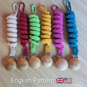 Peut inclure: Six attaches-sucettes crochetés à la main, aux couleurs vives. Chaque attache comprend une perle en bois et une spirale crochetée en blanc, rouge, vert, jaune, violet et bleu. Les noms "Felix", "Gabriel" et "Sacha" sont gravés sur certaines perles.