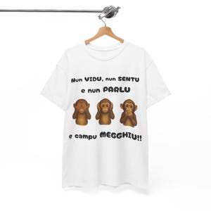 May include: White t-shirt featuring three cartoon monkeys in brown, each in the 'see no evil, hear no evil, speak no evil' pose. The shirt has text above and below the monkeys in a dark font.