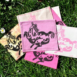 May include: Four fabric squares with a black silhouette of a horse printed on each. The squares are in various shades of pink and beige.