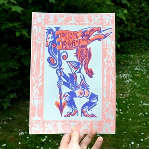 May include: A blue and pink print of a knight holding a banner that says "Pink Pony". The knight is wearing a helmet and armor. The banner is decorated with a pink pony and a red dragon. The print is surrounded by a pink border with a white pattern.