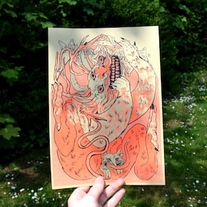 May include: A print of a fantastical creature with multiple eyes and a toothy grin, rendered in shades of orange and pink against a cream background.
