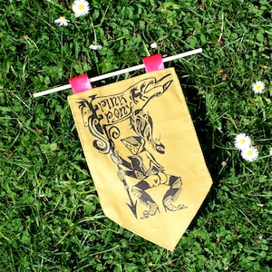 May include: A yellow fabric banner with black lettering that reads "Pink Pony" and a black and white illustration of a person riding a horse. The banner is attached to a white stick with pink ribbon.