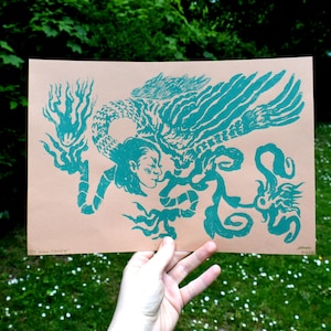 May include: A teal blue print on a light brown paper background. The print features a stylized image of a woman with a bird's head and wings, surrounded by swirling vines. The text "The Sun Sleeps" is printed at the bottom of the image.