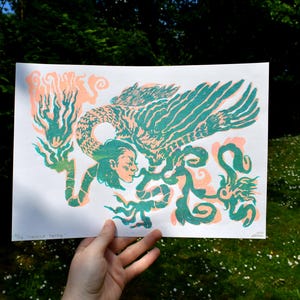 May include: A green and pink linocut print of a mythical creature with a human head and a bird's body. The creature is surrounded by swirling lines and shapes.