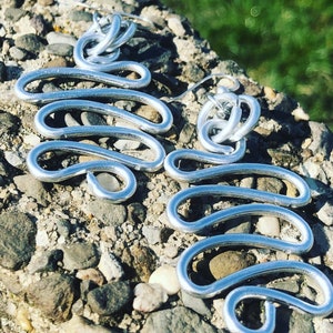 May include: A pair of silver earrings with a wavy, abstract design. The earrings are made of wire and have a simple, modern look.