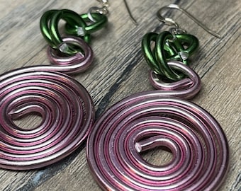 May include: A pair of earrings with a pink spiral design and green chain links. The earrings are made of metal and have a silver hook.