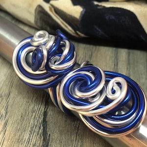 May include: A pair of silver and blue wire rings, twisted and intertwined, creating a unique and intricate design.