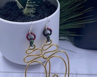 Könnte beinhalten: Goldene Drahtohhringe mit einem einzigartigen, abstrakten Design. Die Ohrringe haben rote, grüne und schwarze Perlen.