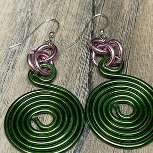 May include: A pair of green and pink wire earrings with a spiral design. The earrings are made of metal wire and have a silver hook.