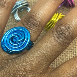K&ouml;nnte beinhalten: Ein t&uuml;rkisfarbener Drahtring mit einem Spiraldesign. Der Ring wird an einem Finger getragen.