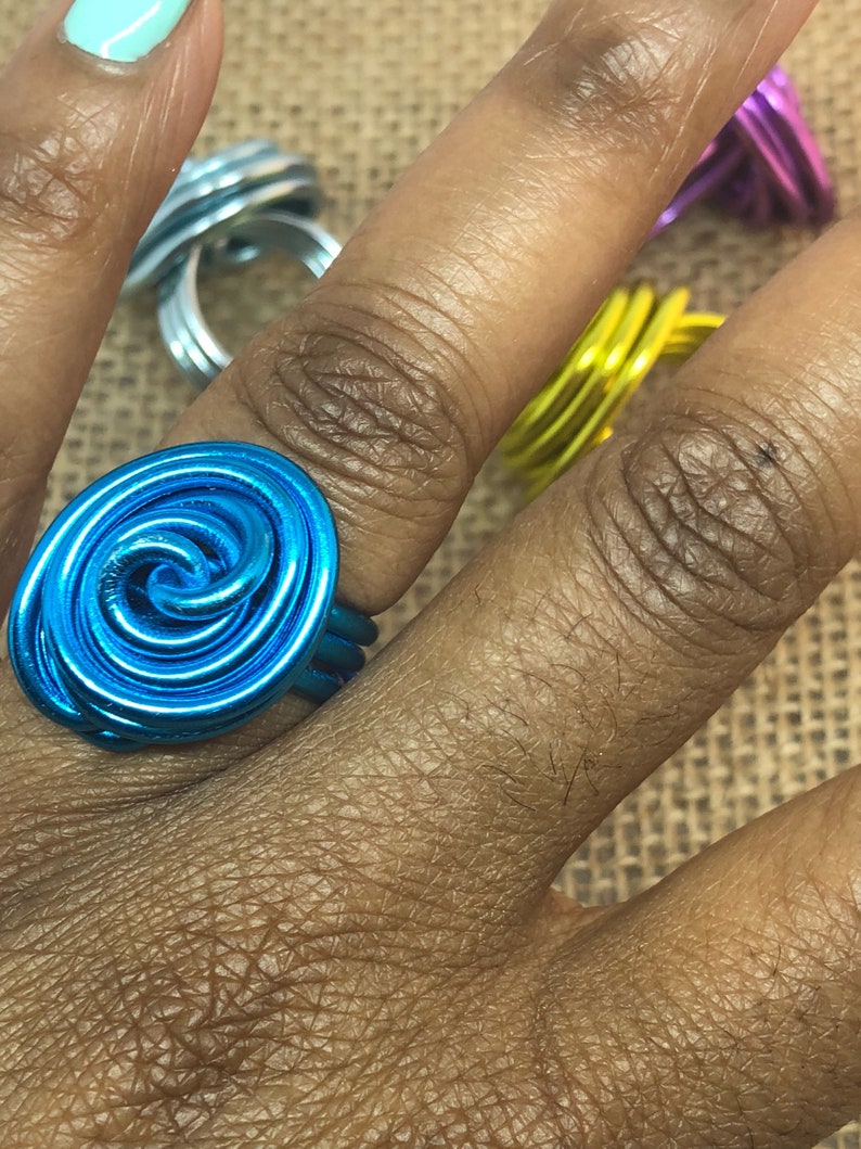 K&ouml;nnte beinhalten: Ein t&uuml;rkisfarbener Drahtring mit einem Spiraldesign. Der Ring wird an einem Finger getragen.