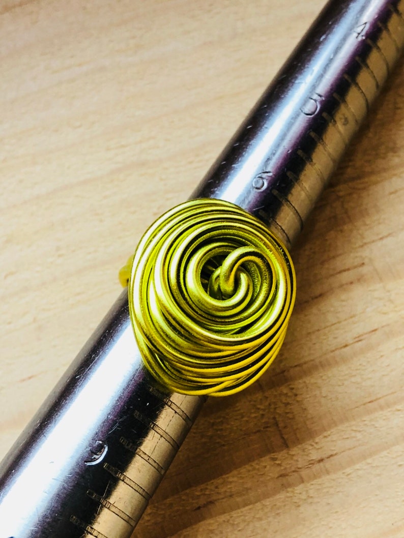 K&ouml;nnte beinhalten: Ein Ring aus lindgr&uuml;nem Draht mit einem Spiraldesign. Der Ring liegt auf einem Metalllineal.