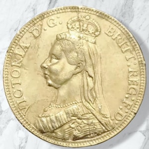 Può includere: Moneta dorata raffigurante il profilo di una donna incoronata, con l'iscrizione "VICTORIA D.G. BRITT. REG. F.D." sul bordo. La moneta è circolare e presenta un rilievo dettagliato.