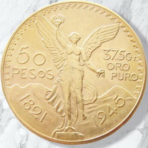 May include: A gold 50 Pesos coin featuring the Winged Victory of Samothrace statue. The coin displays the text 50 PESOS, 37.5G ORO PURO, 1821, and 1945. The design includes a winged figure holding a laurel wreath and a broken chain.