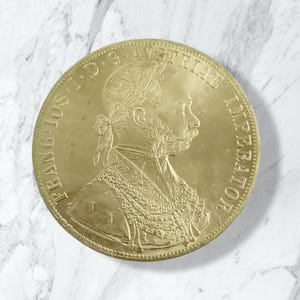 Puede incluir: Una moneda de oro con el perfil de un hombre con una corona de laurel y barba. La moneda tiene la inscripción "FRANC IOS I D G AUSTRIAE IMPERATOR". La moneda es redonda y tiene un diseño detallado. Diámetro aproximado de 3,8 cm.