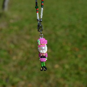 May include: A beaded Santa Claus pendant with a silver clasp. The Santa figure is made of pink, white, black, green, and gold beads. The necklace chain is made of red, green, and white beads.