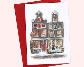 May include: Watercolor greeting card featuring two historic buildings with snow-covered roofs and a street lamp. The buildings have red shutters and doors, with festive decorations in the windows. The card is set against a red background.