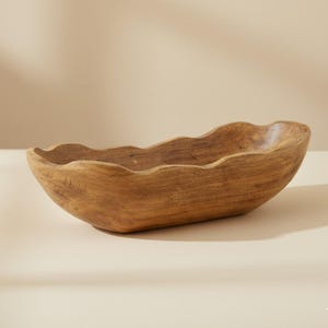 May include: A handcrafted wooden bowl with a wavy rim. The bowl is oval-shaped and made of light brown wood. The natural wood grain is visible, adding texture and character to the piece. This decorative bowl is suitable for serving or display.