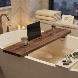 May include: A walnut-colored wooden bathtub tray featuring a slot for a tablet or phone, a circular cutout for a wine glass, and a circular indentation for a candle. The tray includes a sign reading 35" L Wood Bathtub Tray with Wine and Tablet/Phone Slot, Walnut Color.