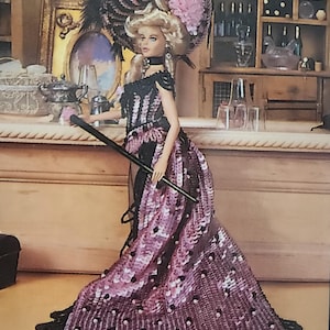May include: A doll dressed in a detailed, vintage-style outfit. The doll wears a black and pink sequined gown with a matching hat adorned with feathers and a pink flower. She holds a black cane, set against a bar-like background.
