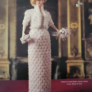May include: A doll dressed in a white beaded evening suit, including a bolero jacket and a long dress. The doll is holding a bouquet of flowers and a small purse. The text on the image reads "PRINCESS DIANA 1989 BEADED EVENING SUIT."