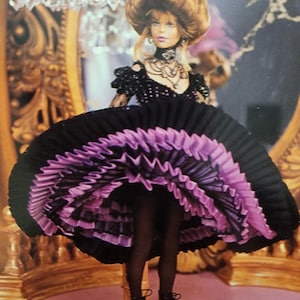 Puede incluir: Una muñeca con un vestido negro y morado con una falda con volantes. La muñeca tiene el pelo castaño y lleva zapatos negros.